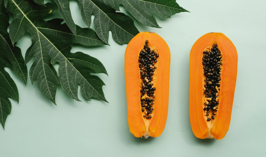 Top view of freshly halved papayas with leafy background, highlighting tropical freshness.