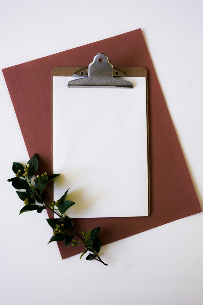 Top view of a clipboard on brown paper with green leaves. Minimalist and elegant composition.