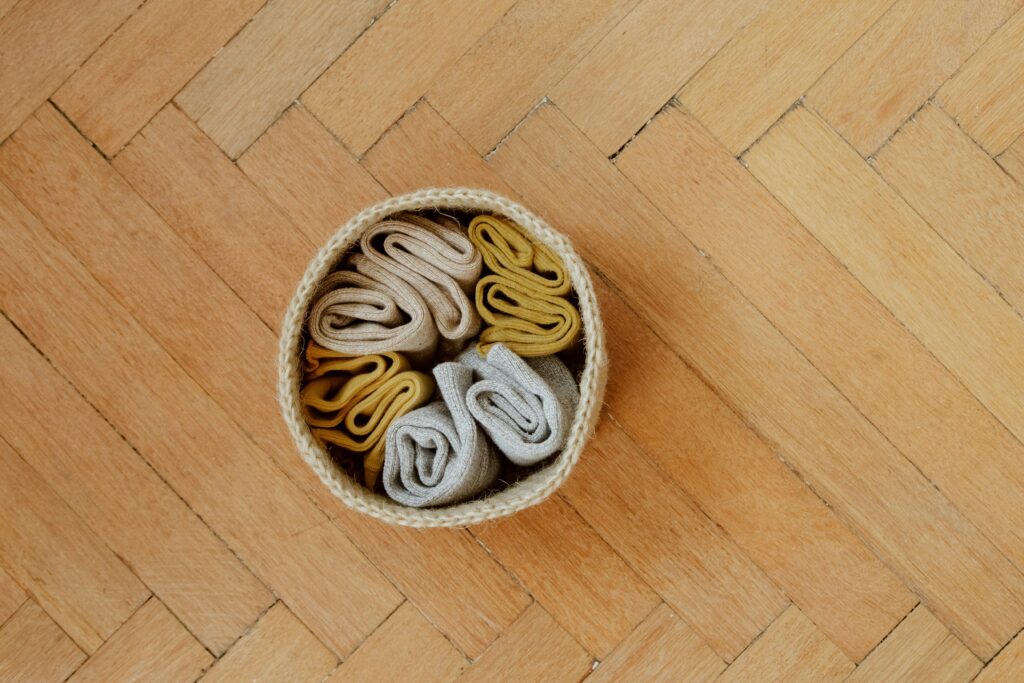 Top view of neatly organized socks in a wicker basket on a parquet floor, showcasing minimalist home organization.