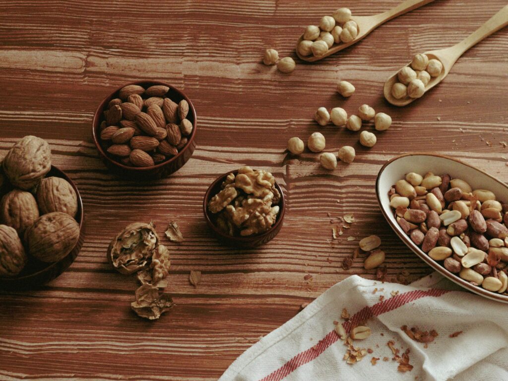 A top view of various nuts in bowls and spoons on a wooden tabletop.