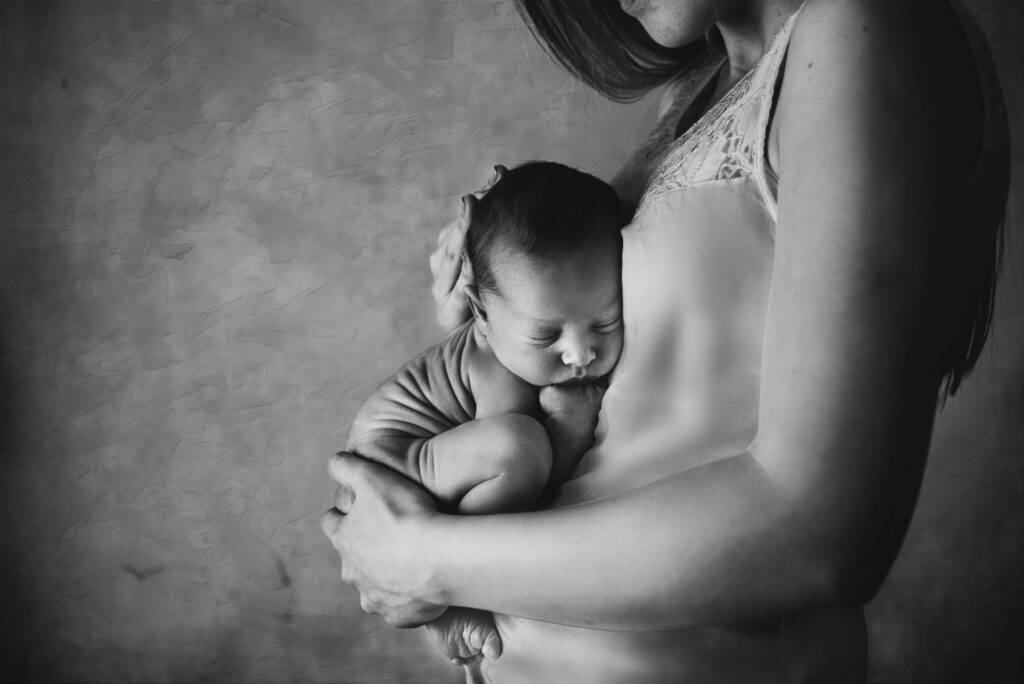 A touching black and white image of a mother gently holding her sleeping newborn close.