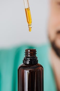 A dropper with golden oil suspended above an open amber bottle, close-up view.