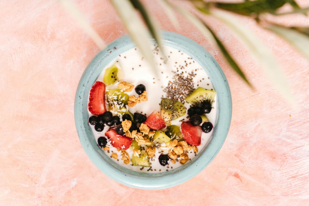 Top view of a healthy breakfast bowl with yogurt, fruits, and seeds on a pink background.