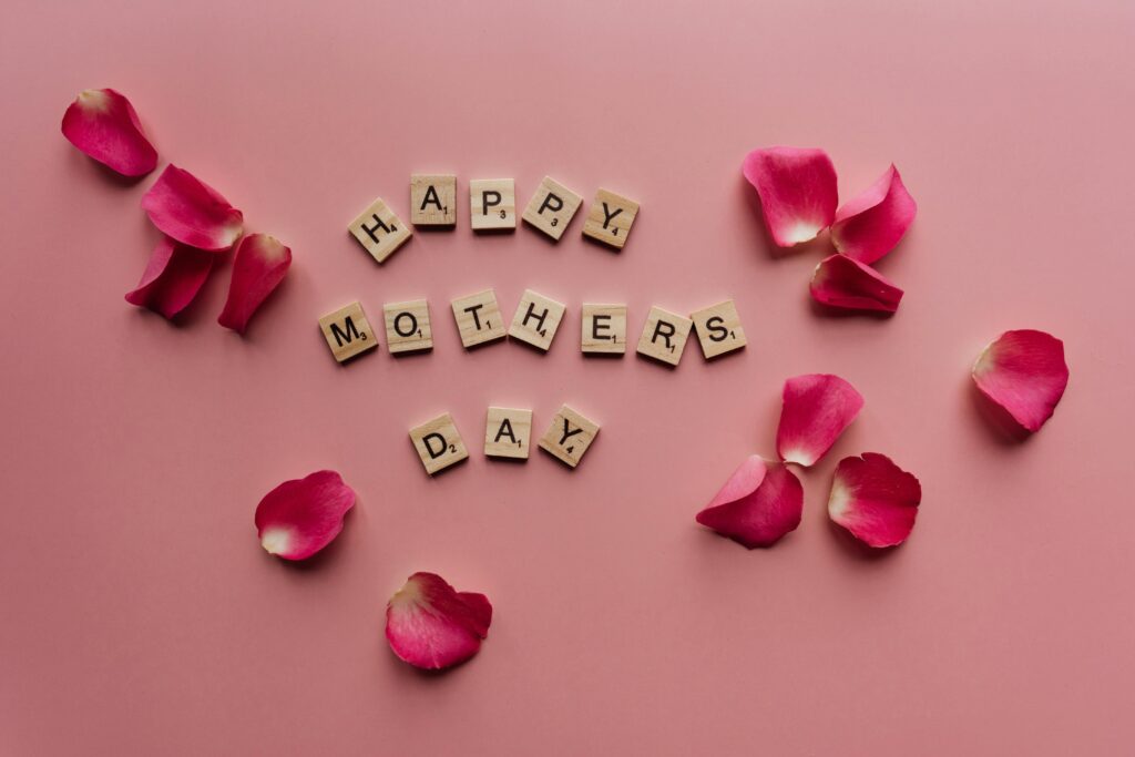 Scrabble tiles spelling 'Happy Mother's Day' surrounded by pink petals.