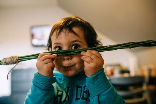 A cute child with brown hair posing playfully indoors with green sticks.